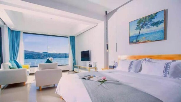 A modern hotel room with a large bed, a sofa, a TV, and a painting of a tree by a lake. - Shuanglang Ziyan Zhuangyuan Inn (Dali City)