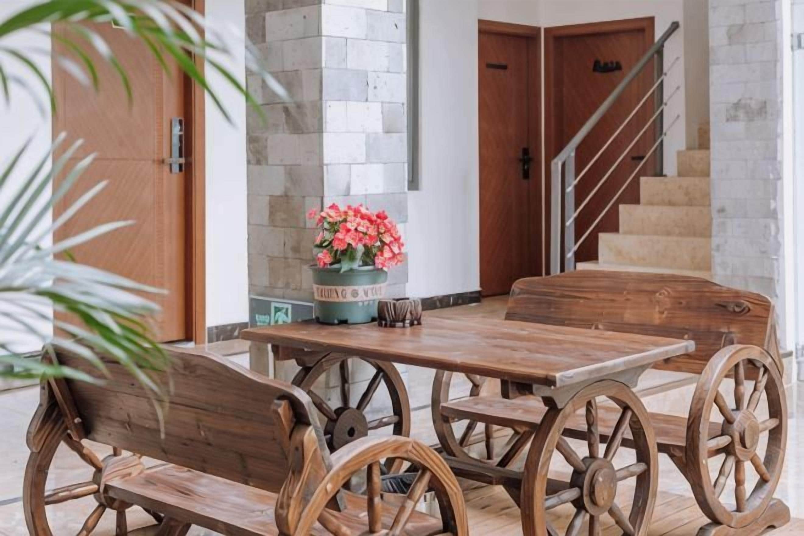 Una mesa de madera con sillas, un florero y una escalera al fondo.