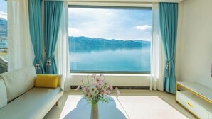 A modern room with a large window, a sofa, a small table with a vase of flowers, and a TV on the wall. - Shuanglang Ziyan Zhuangyuan Inn (Dali City)