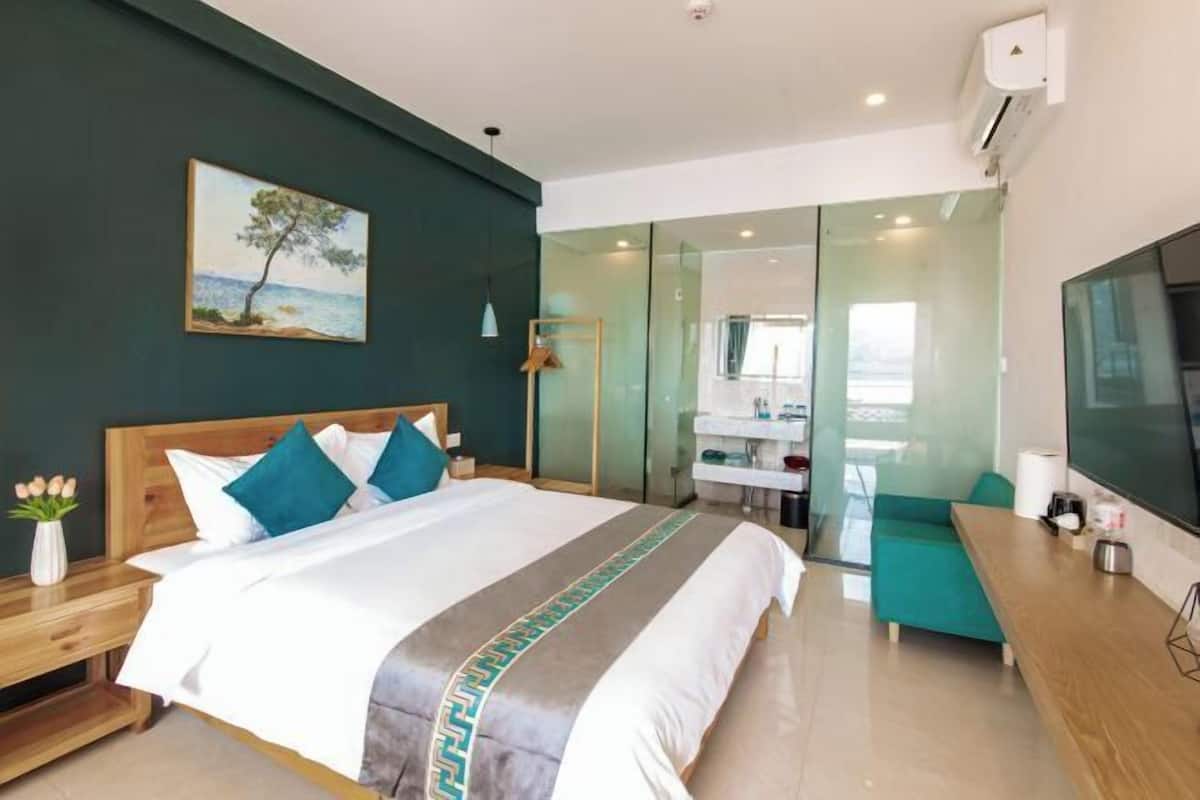 A modern hotel room with a bed, a desk, a TV, a bathroom, and a painting on the wall.