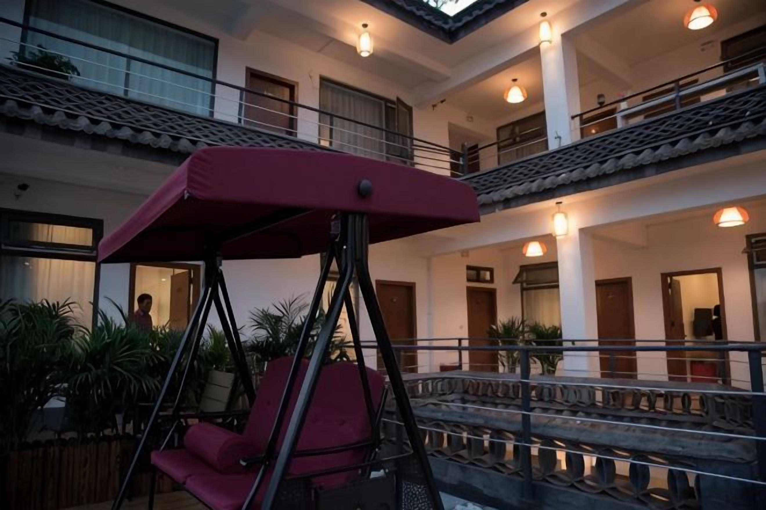 Een meerlaags gebouw met een schommelstoel op de voorgrond, een balkon op het bovenste niveau en een leuning met verlichting.