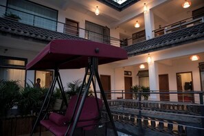Un immeuble à plusieurs étages, avec une chaise suspendue en premier plan, un balcon à l’étage supérieur et une rambarde ornée de lumières.