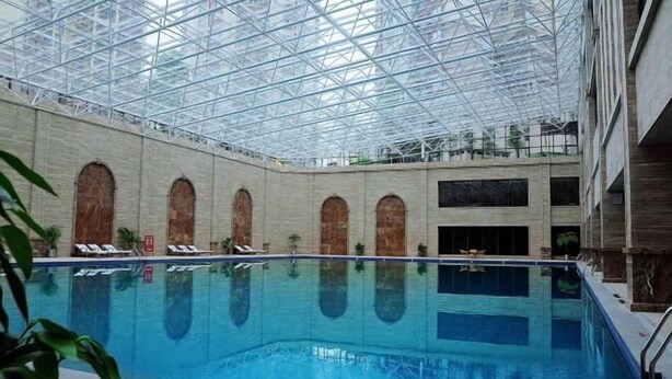 Une piscine intérieure dotée d’un toit en verre, de fenêtres en arc de cercle et de chaises longues.