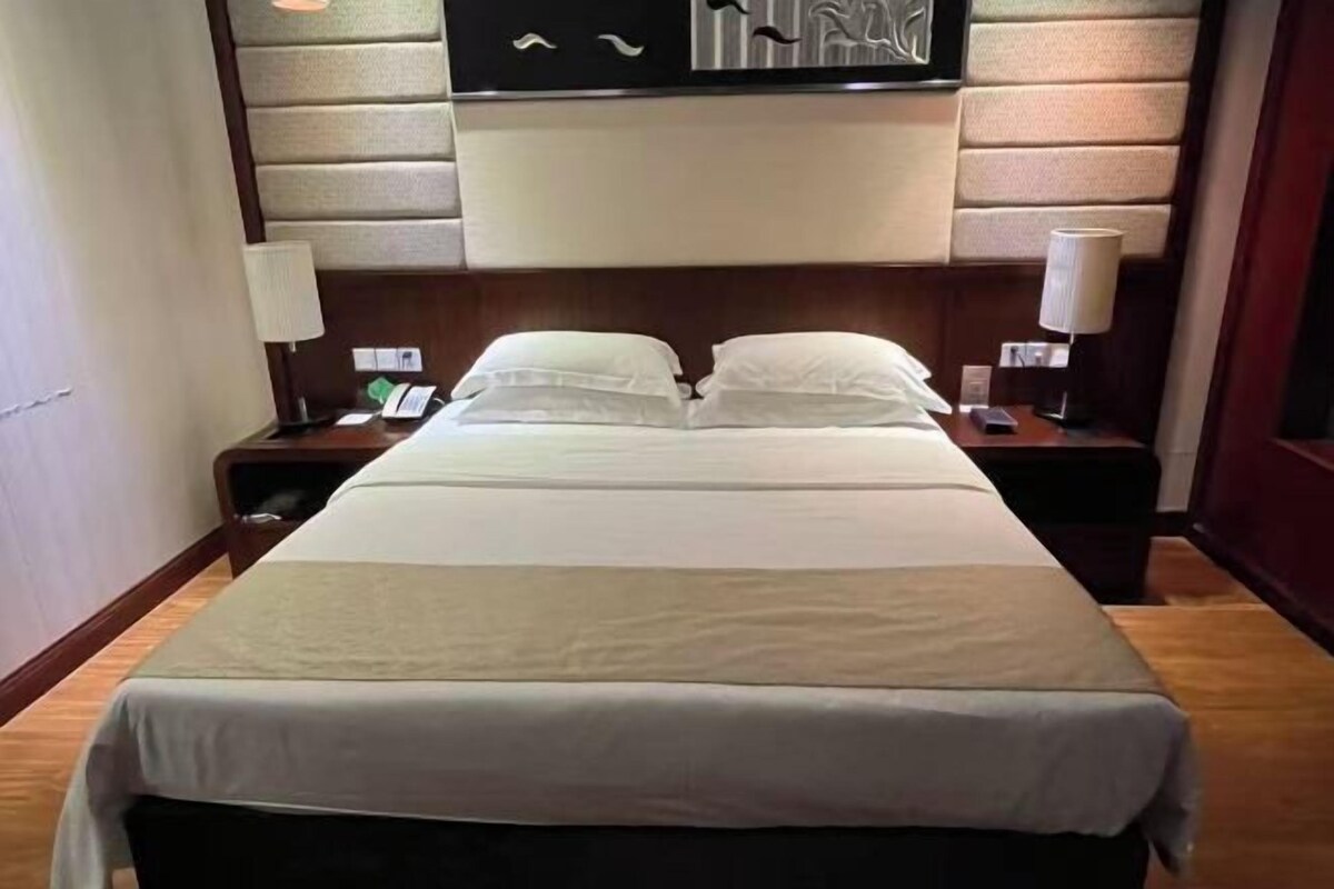 Ein Hotelzimmer mit einem großen Bett, zwei Nachttischen und einem an der Wand befestigten Fernseher.