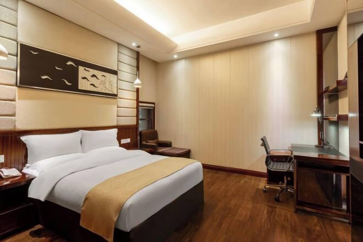 Habitación de hotel con una cama grande, un escritorio con silla, una lámpara de escritorio, un teléfono y una obra de arte colgada en la pared.