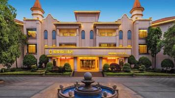 A hotel with a central entrance, a fountain in the courtyard, and a well-maintained garden.