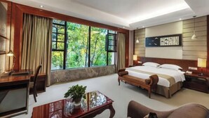 Une chambre d’hôtel avec une grande fenêtre, un lit, un bureau, une chaise et une table de chevet.