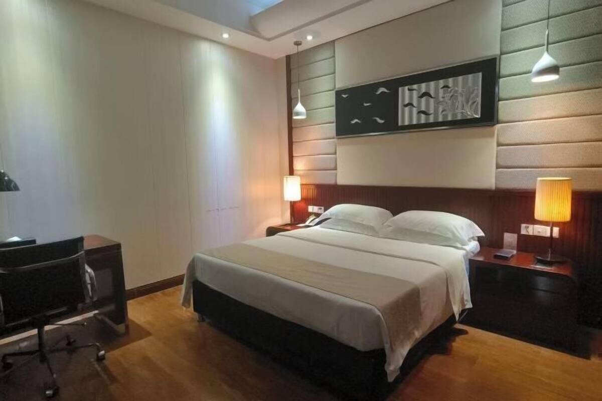 Una habitación de hotel con cama, lámparas de noche, un escritorio con silla y una obra de arte colgada en la pared.