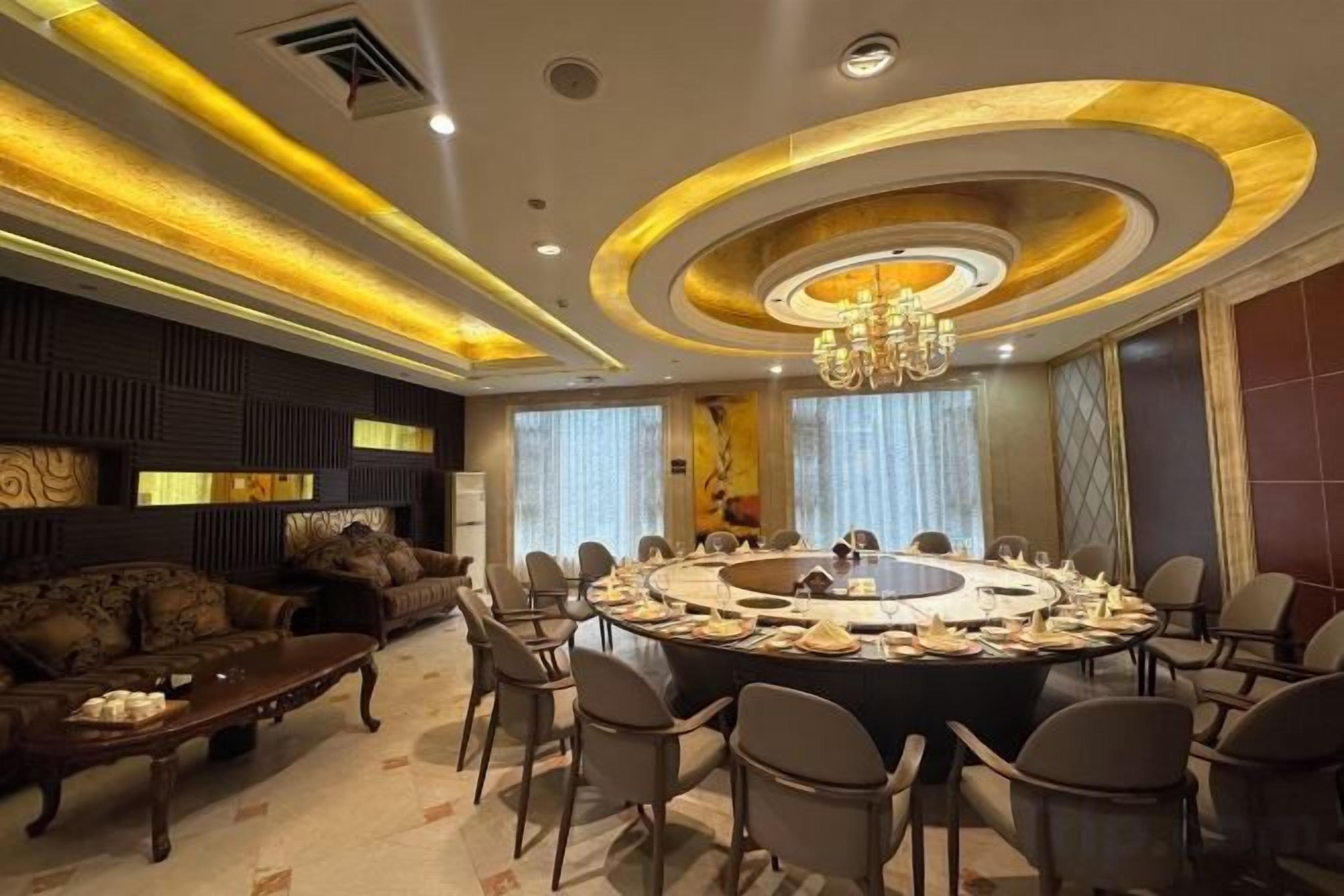 A modern dining area with a round table surrounded by chairs, a chandelier, and a sofa set.