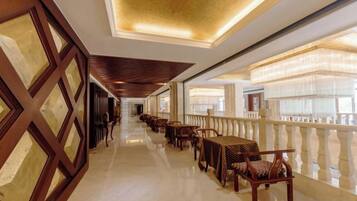 A corridor with tables and chairs, a railing, and a ceiling with a patterned design.