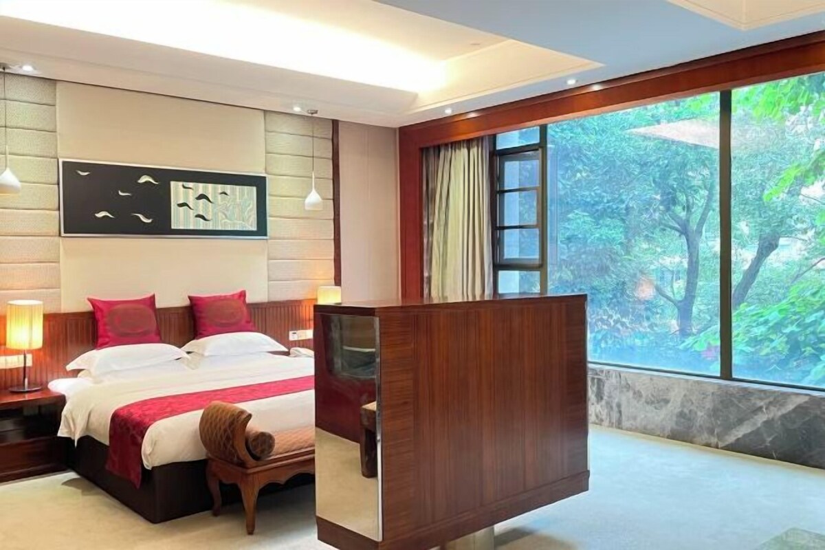 Ein modernes Hotelzimmer mit einem großen Bett, Nachttischen, einem Spiegel und Blick auf Grünflächen.