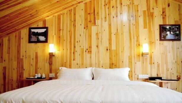 A room with a wooden slat wall, a large bed with white bedding, two bedside tables with lamps, and two framed pictures on the wall. - Meilaiya Hotel Huangyao Ancient Town (Zhaoping)