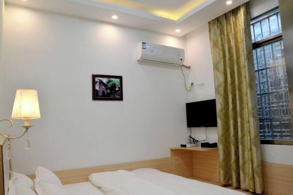 A hotel room with a bed, a bedside lamp, an air conditioning unit, a television, and a window with curtains.