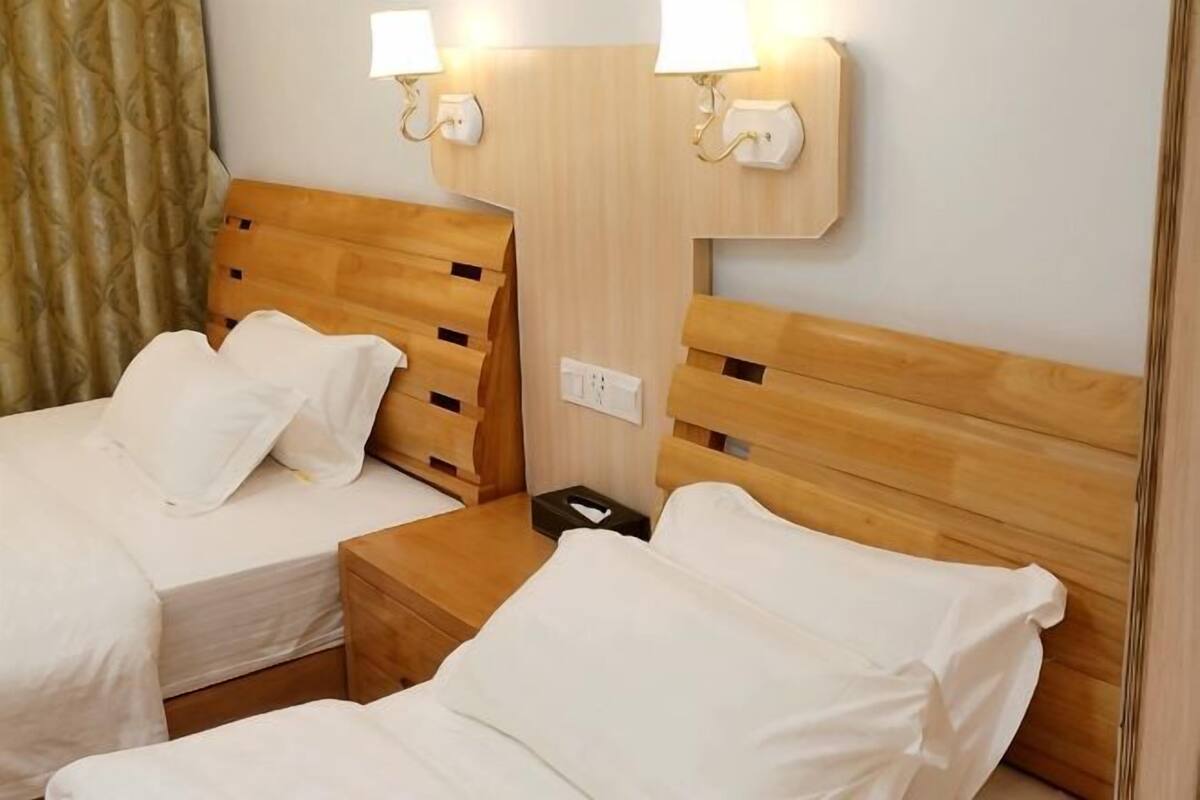 A hotel room with two beds, wooden headboards, bedside lamps, and a nightstand.