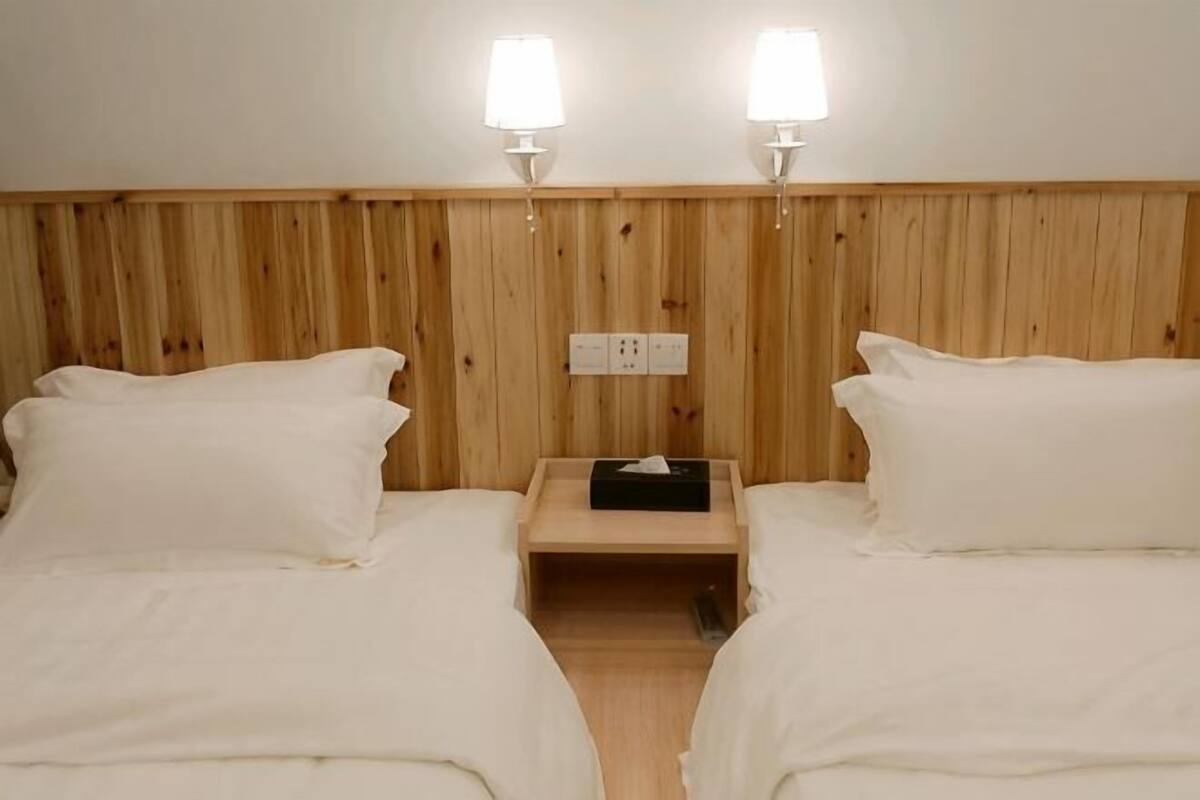 A room with two beds, wooden headboard, bedside lamps, and a nightstand with a lamp.