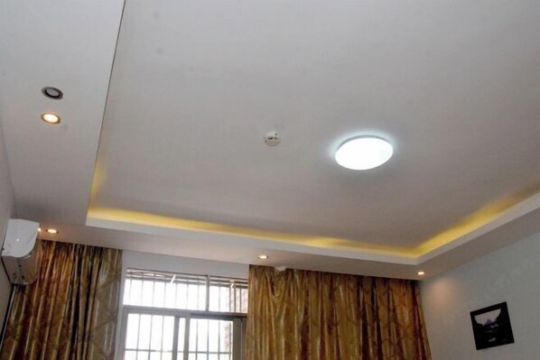 Une pièce avec un plafond blanc, des spots encastrés, une fenêtre grillagée et un climatiseur fixé au mur.