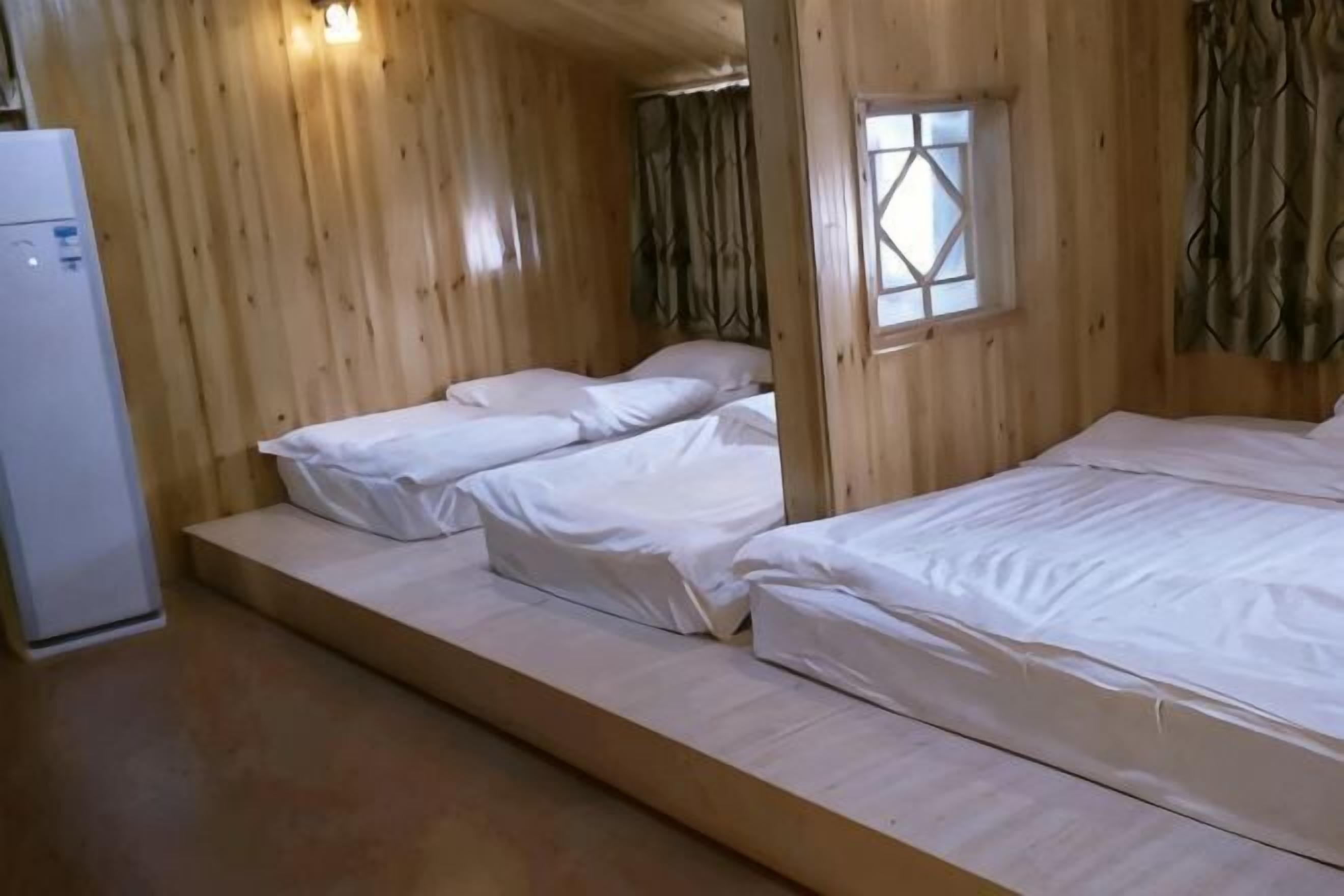 Eine Holzhütte mit zwei Betten, einem Fenster und einem Kühlschrank.