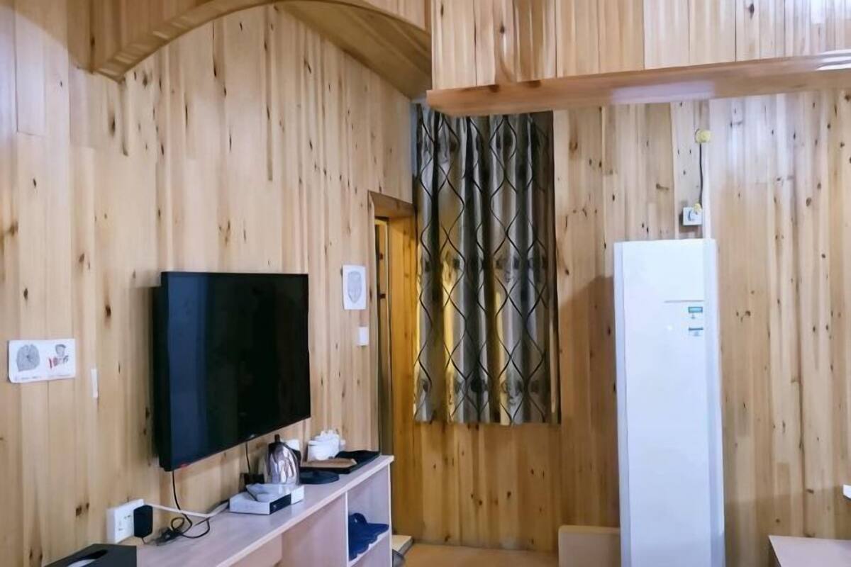 A wooden-paneled room with a flat-screen TV, a white refrigerator, and a door with a patterned curtain.