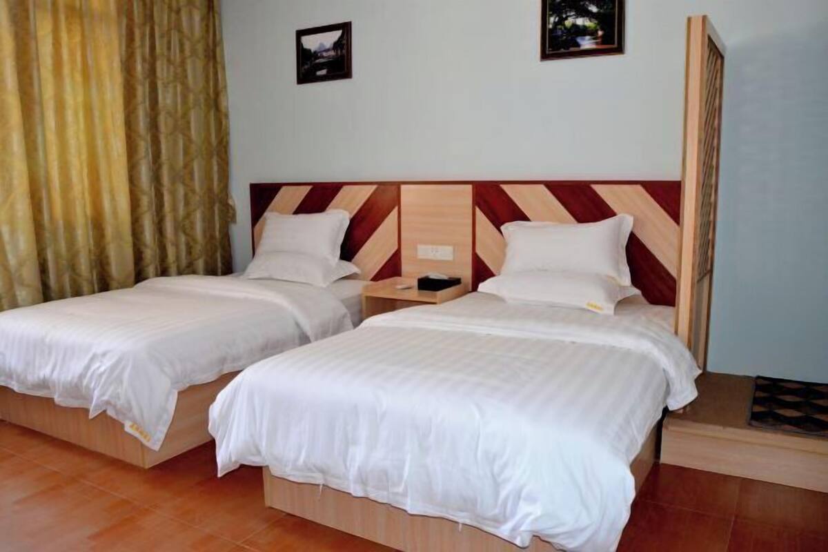 A hotel room with two beds, a wooden headboard, a nightstand, and a wall-mounted picture.