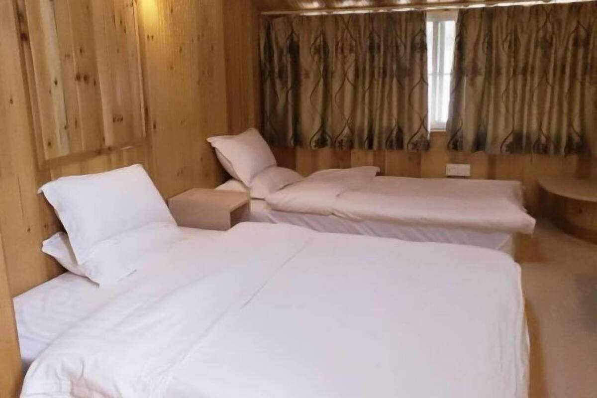 A room with two beds, wooden walls, and a window with curtains.