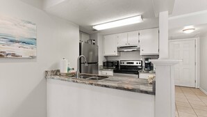A modern kitchen with white cabinets, stainless steel appliances, and a marble countertop.