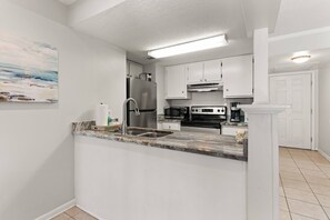 A modern kitchen with white cabinets, stainless steel appliances, and a marble countertop. - Beachfront Condo | Pet Friendly | Pool | Kids Bikes | Beach Gear | Elevator | Covered Parking (St. Simons Island)