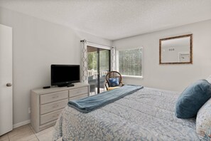 A bedroom with a bed, a television on a dresser, a chair, and a window with blinds. - Beachfront Condo | Pet Friendly | Pool | Kids Bikes | Beach Gear | Elevator | Covered Parking (St. Simons Island)