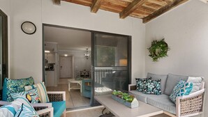 A modern living room with a sofa, chairs, and a coffee table. There is a sliding glass door leading to a kitchen and dining area.