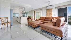 A modern living room with a large brown leather sofa, a dining area with a table and chairs, and a kitchen in the background. - Skytower Wonder Oceanview Balcony - Pool - Office (Darwin)