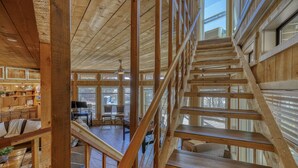 A wooden interior with a staircase, large windows, and a dining area.