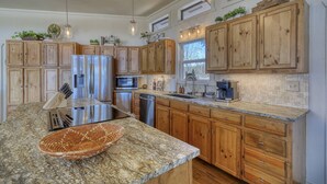 A kitchen with wooden cabinets, granite countertops, stainless steel appliances, and pendant lighting.