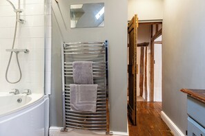 A bathroom with a bathtub, a towel rack with two towels, a shower head, and a mirror on the wall. - Clifford Chambers Cosy 2 Bedroom Cottage (Stratford-upon-Avon)