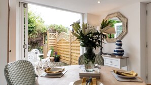 A dining area with a table set for two, a vase with flowers, a mirror, and a wooden fence in the background. - Clifford Chambers Cosy 2 Bedroom Cottage (Stratford-upon-Avon)