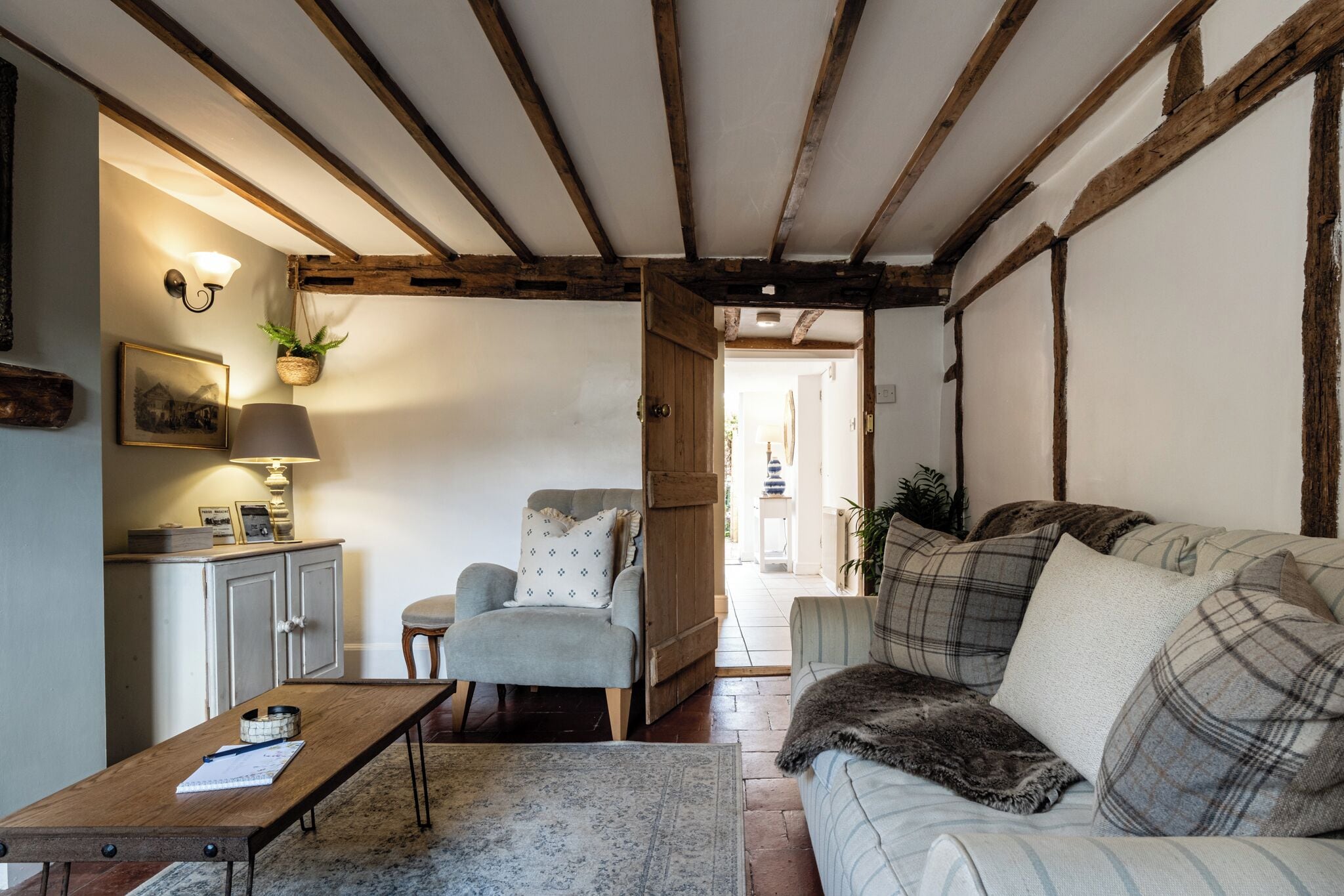 A cozy living room with a wooden ceiling, a sofa with plaid cushions, a wooden coffee table, a chair, and a lamp.