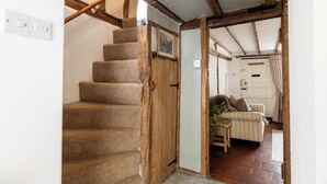 A staircase with wooden beams, a white door, and a room with a striped sofa and a radiator. - Clifford Chambers Cosy 2 Bedroom Cottage (Stratford-upon-Avon)