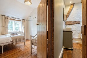 A bedroom with a wooden bed, a window with curtains, a white radiator, and a wooden wardrobe. - Clifford Chambers Cosy 2 Bedroom Cottage (Stratford-upon-Avon)
