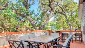 A deck with a table and chairs, surrounded by trees and a view of a building. - Relax, Swim & Explore: Home in Wimberley! (Wimberley)