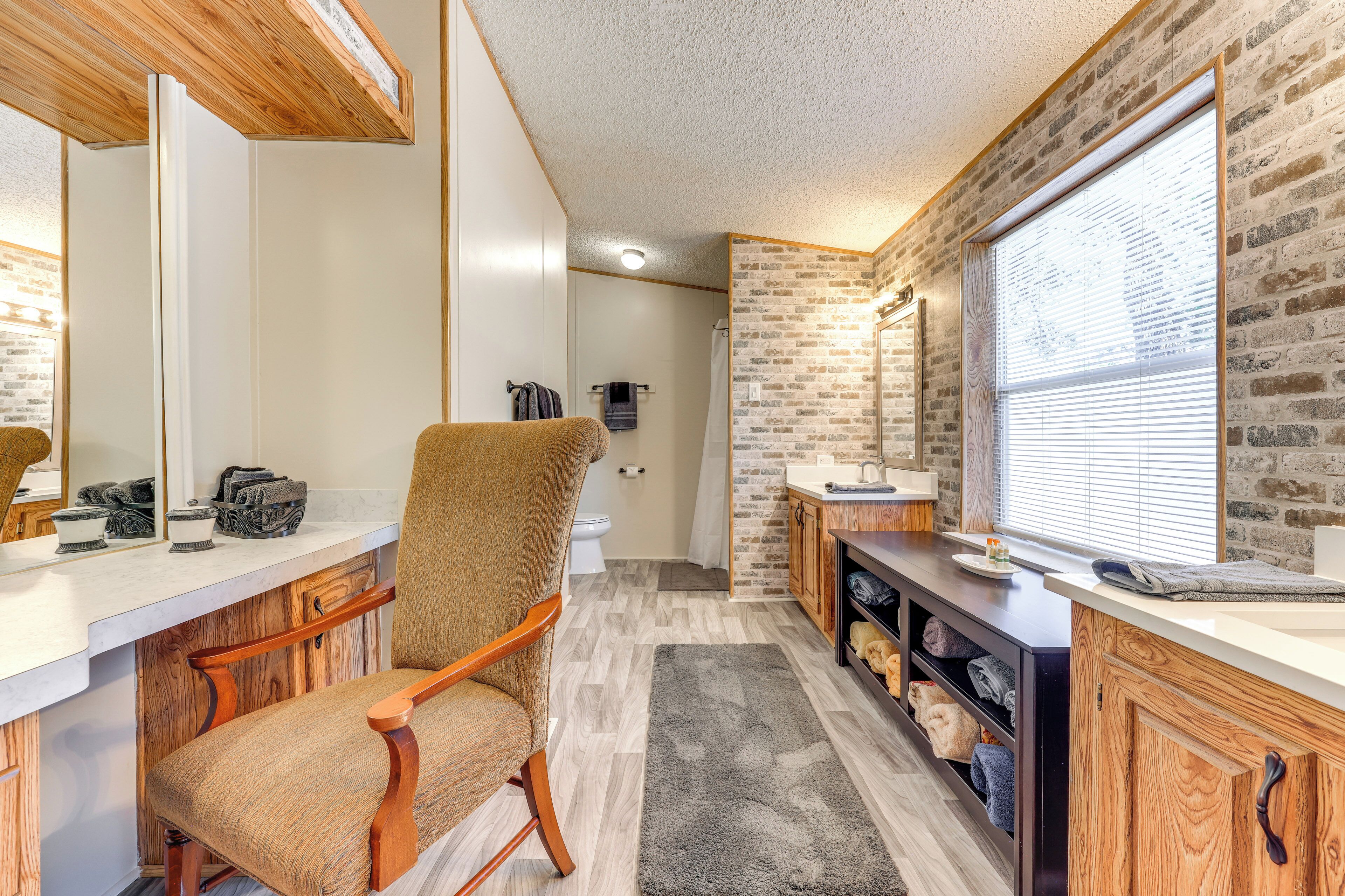 A modern bathroom with a wooden vanity, a chair, and a large window.