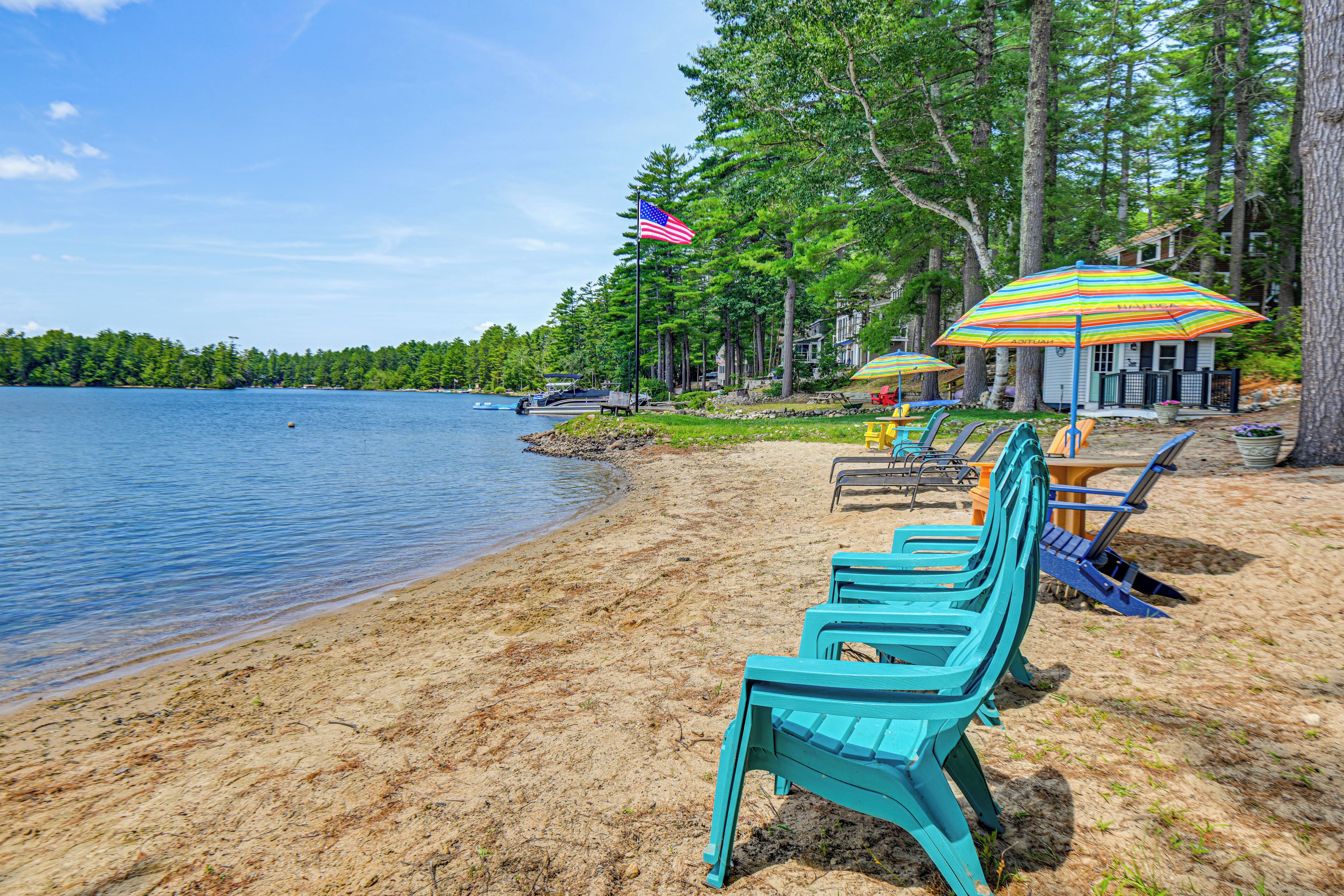 A beach with turquoise chairs, a flag, and a striped umbrella.