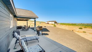 Eine überdachte Terrasse mit Gartenmöbeln, einem Grill und Blick auf eine ländliche Landschaft.