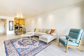 Una sala de estar moderna con un sofá seccional de color claro, un sillón azul, una alfombra estampada y una pequeña mesa de centro.