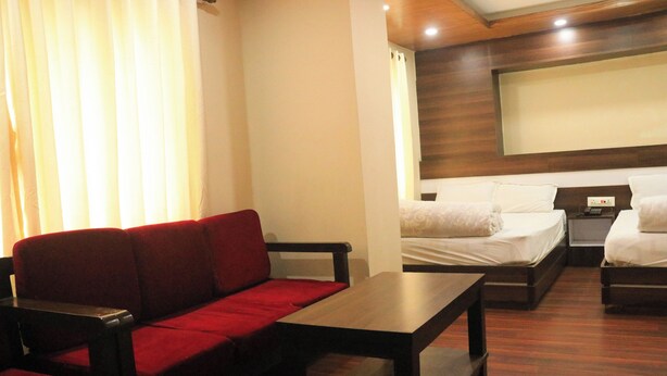 A hotel room with a red sofa, a wooden table, two single beds, and a large mirror on the wall. - Pashupati Hotel  (Kathmandu)