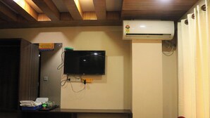 A room with a flat-screen TV mounted on the wall, an air conditioning unit, a desk with a tray of toiletries, and a red chair. - Pashupati Hotel  (Kathmandu)