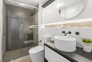 Features a sleek bathroom with a large round sink, glass-enclosed shower, and minimalist vanity.