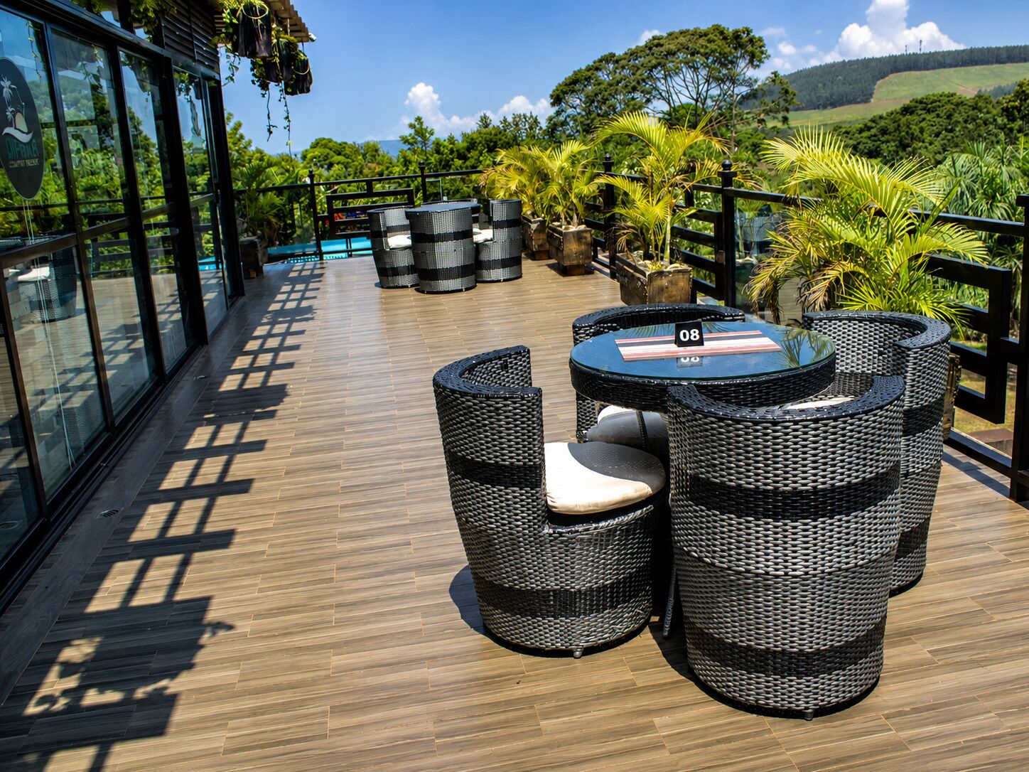 An outdoor seating area with wicker furniture and a table, overlooking a pool and lush greenery.