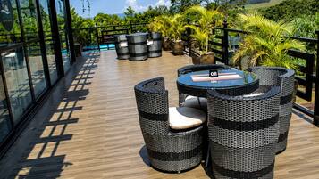 An outdoor seating area with wicker furniture and a table, overlooking a pool and lush greenery.