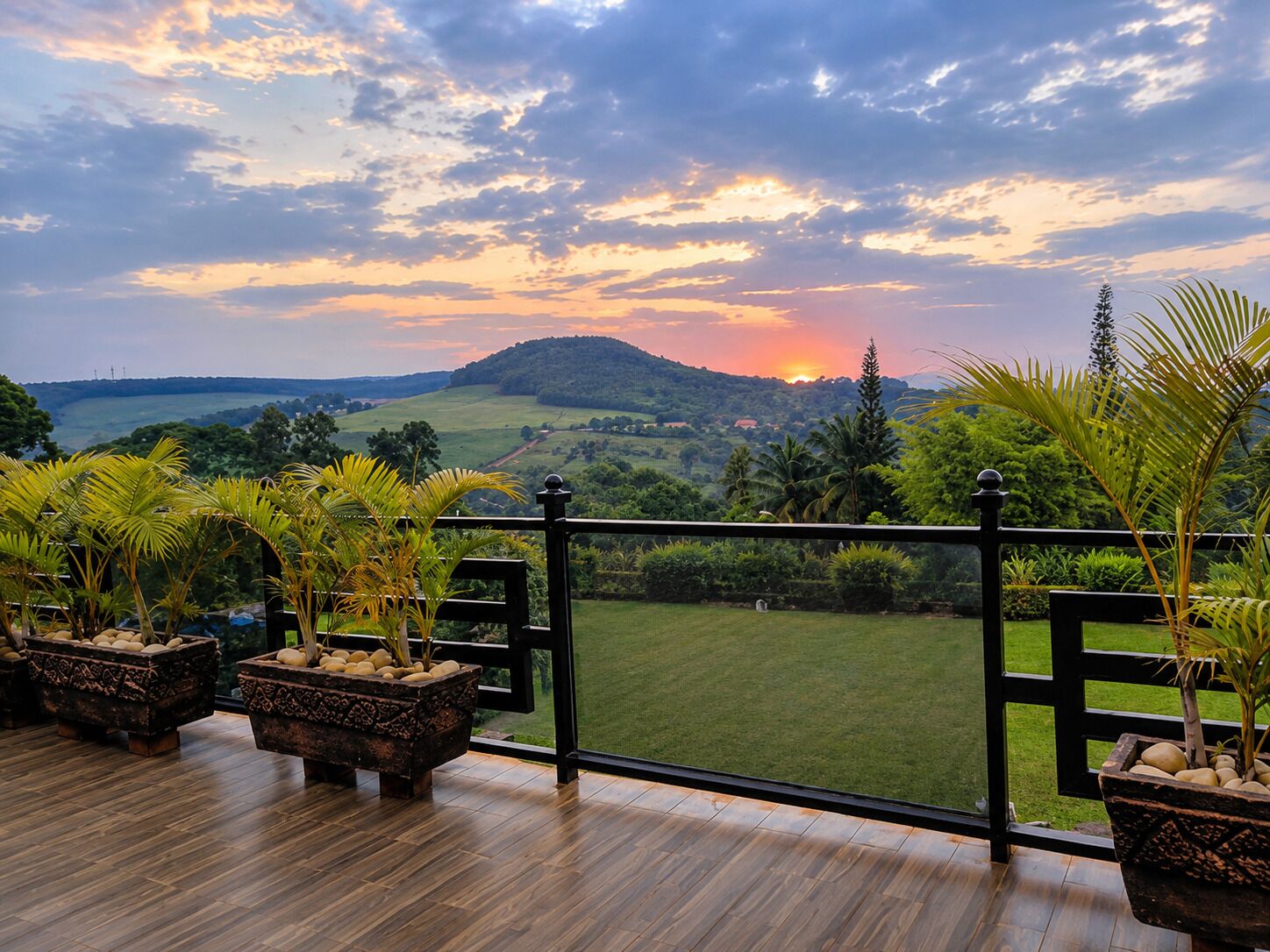 Un balcone con vista su un tramonto su un paesaggio collinare, pavimento in legno e fioriere decorative.