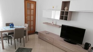 Ein modernes Wohnzimmer mit Fernseher, Holzschrank und Essbereich mit Tisch und Stühlen.