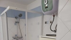 Eine Dusche mit Handbrause und Wandarmatur, eine Toilette sowie ein Schrank mit Tür.