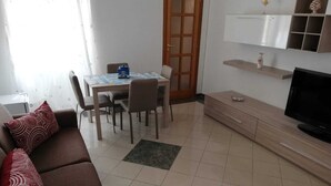 Ein Wohnzimmer mit einer Couch, einem Esstisch mit Stühlen, einem Fernseher und einem Schrank.